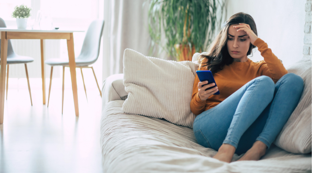 Worried woman sitting on couch looking at phone while searching for a rental in Australia