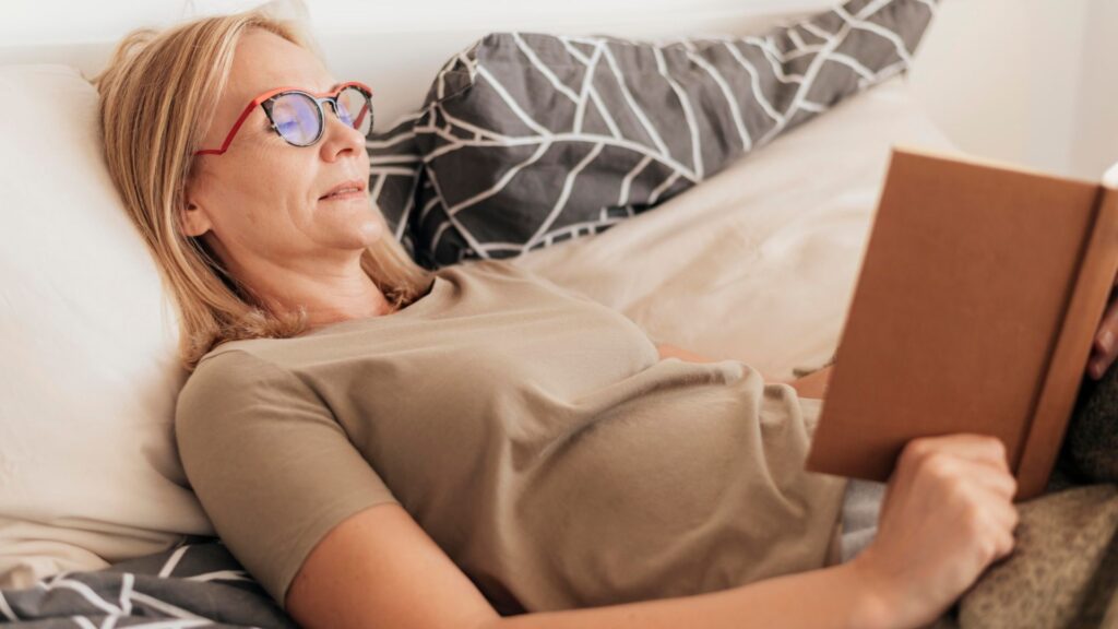 Senior woman reading in bed while reflecting on whether she is ready to retire and what retirement readiness looks like